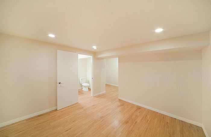 Spacious room with modern recessed lighting and hardwood flooring, featuring a bright white painted door leading to an adjacent bathroom.