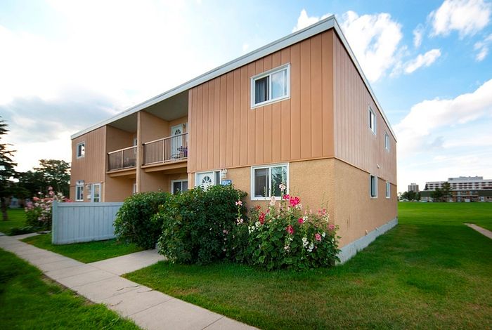 Charming apartment building with spacious balconies, surrounded by lush greenery and vibrant flowers, perfect for community living.