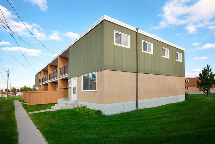 Modern apartment building with a green facade, surrounded by lush grass and a clear blue sky.