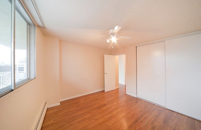 Bright and airy bedroom with elegant wooden floors, large window, and sleek ceiling fan.