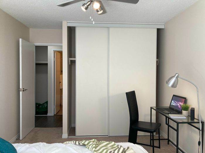 Modern bedroom with sleek closet doors, a cozy workspace with a laptop, and soft lighting for a perfect study or relaxation environment.