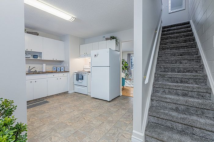 Inviting apartment kitchen with modern white cabinets, plush carpeted staircase, and a glimpse into a cozy living room filled with natural light.