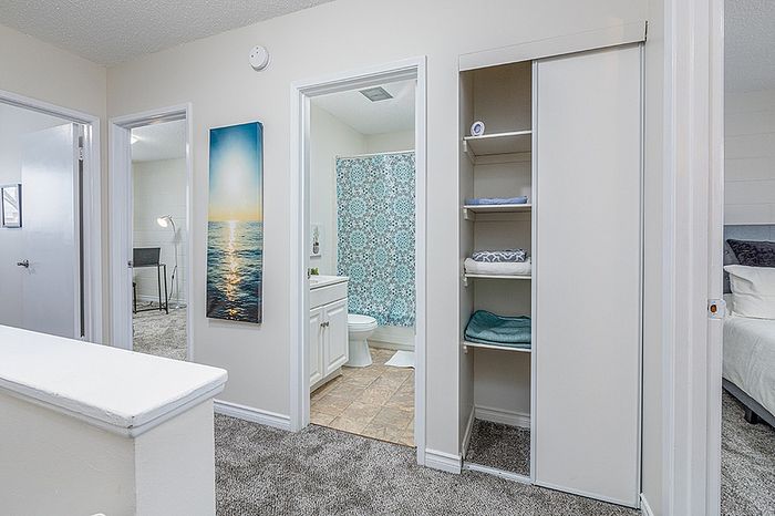 Bright hallway with plush carpet leading to a cozy bedroom, stylish bathroom, and practical storage space, featuring calming artwork and modern decor.