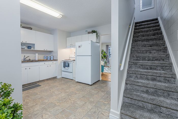 Inviting kitchen with modern white cabinetry and appliances, adjacent to a cozy living room and carpeted staircase.