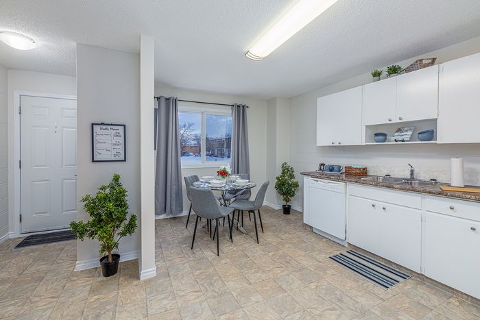 Bright and inviting kitchen and dining area with modern decor, featuring a glass-topped dining table, sleek gray chairs, and ample white cabinetry.