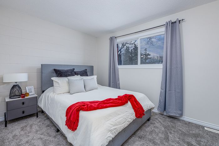 Cozy bedroom with a plush bed, elegant gray curtains, and a large window offering serene outdoor views, accented with a vivid red throw blanket.