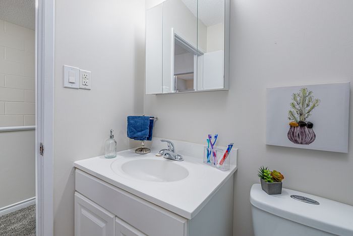 Bright and modern bathroom featuring a sleek white vanity with a stylish faucet, accented by a decorative wall art piece and colorful toothbrushes for a refreshing touch.