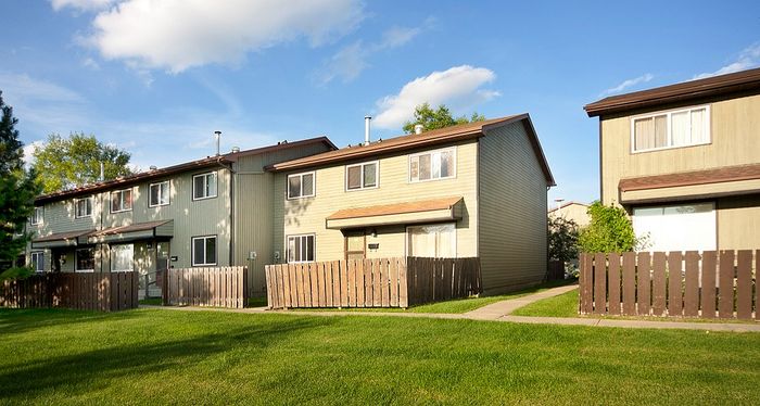 Charming townhouse complex with private fenced yards, surrounded by lush greenery under a bright blue sky.