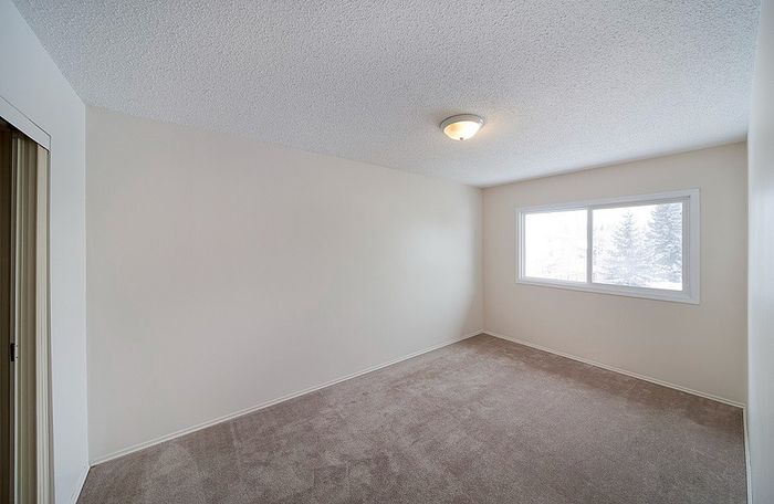 Bright and inviting bedroom with large window, plush carpet, and neutral tones offering a serene atmosphere.