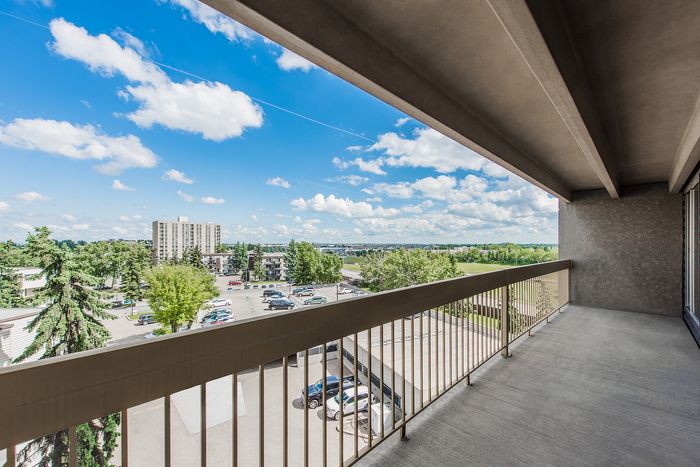 Inviting apartment balcony offering expansive views of lush greenery and a vibrant blue sky, perfect for relaxation.
