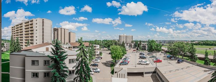 Bright panoramic view of modern apartment buildings surrounded by lush greenery and ample parking under a clear blue sky.