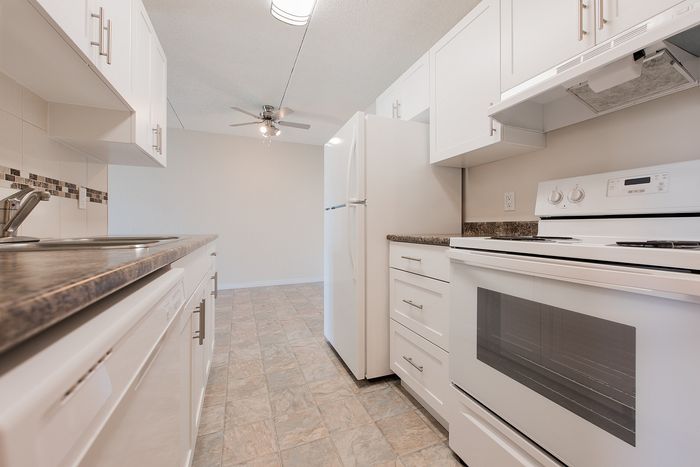 Modern kitchen featuring sleek white cabinetry, spacious countertops, and stainless steel appliances with ambient overhead lighting.