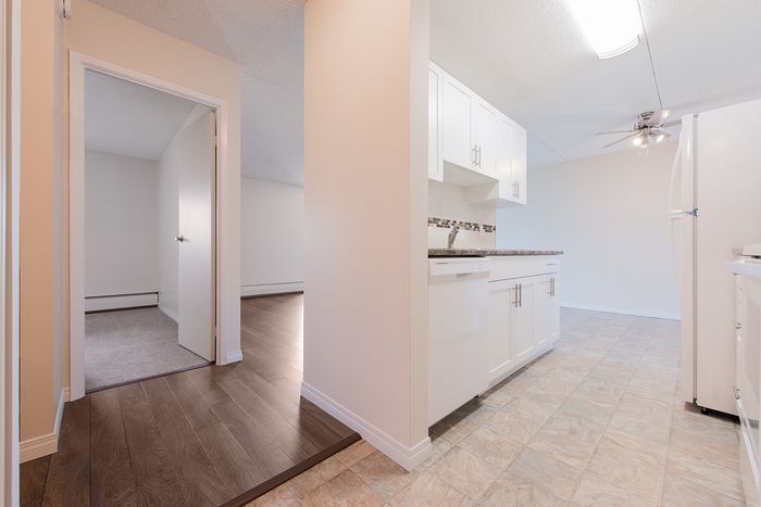 Bright apartment entrance showcasing elegant wood flooring and a modern kitchen with sleek white cabinetry.