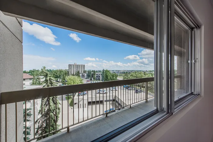 Panoramic view from a spacious balcony overlooking lush greenery and a clear blue sky, offering serenity and natural beauty.