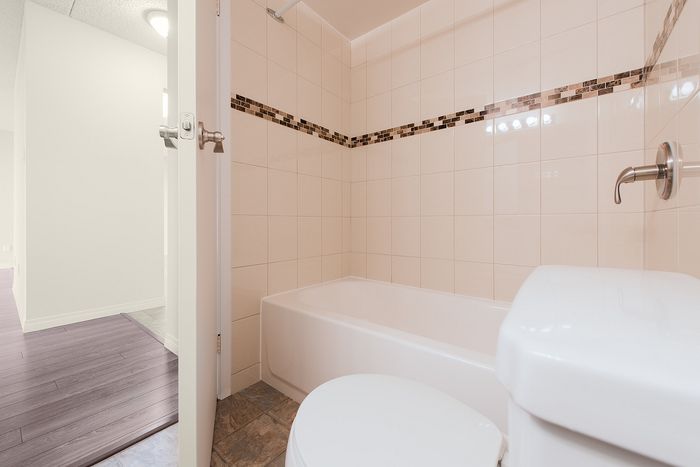 Modern bathroom with elegant beige tiles, sleek bathtub, and stylish mosaic accent trim.