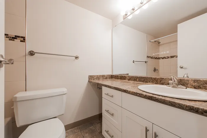 Modern bathroom with elegant granite countertop, sleek white cabinetry, and stylish tile accents.