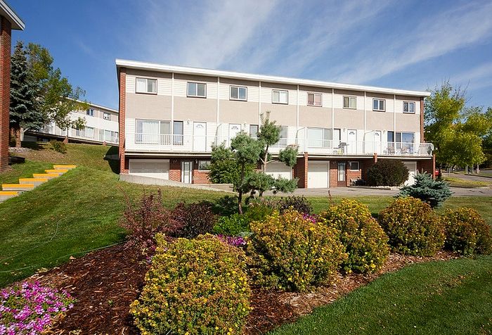 Charming townhouse exterior with lush landscaping and vibrant greenery under a clear blue sky.