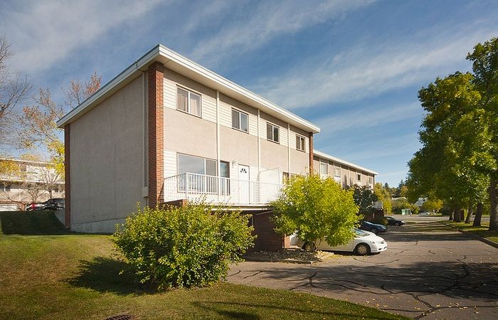 Charming two-story apartment building with brick accents, nestled in a lush, tree-lined neighborhood, offering ideal suburban living.