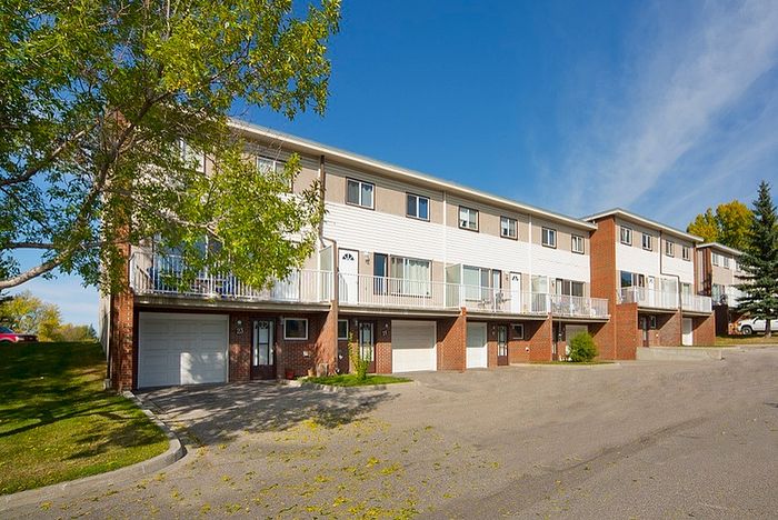 Charming townhouse complex featuring multiple units with private garages and balconies, nestled in a serene suburban setting with lush greenery.