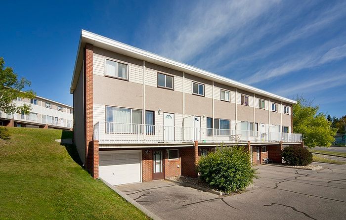 Charming row of modern townhouses with large windows and attached garages, set against a serene blue sky.