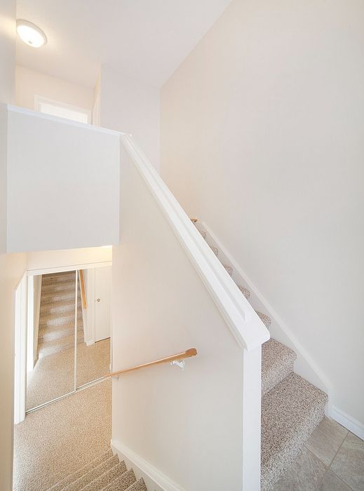 Bright and inviting staircase with elegant white railings and mirrored closet doors, providing a sense of spaciousness and style.