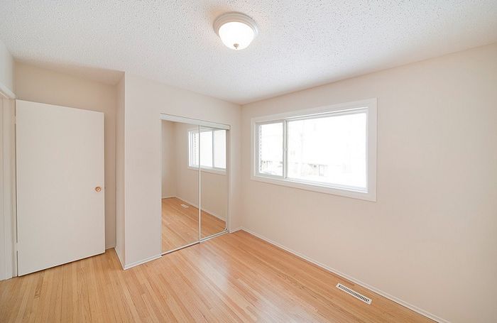 Bright and inviting empty room with wooden floors, a large window, and a mirrored closet door.