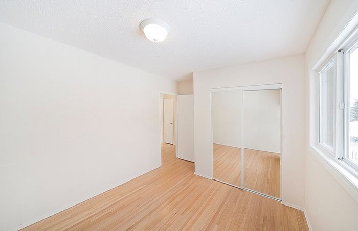Bright, inviting bedroom with hardwood floors, mirrored closet, and natural light streaming in through large windows.