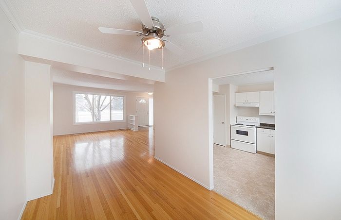 Bright, open-concept living and dining area with polished hardwood floors and a modern kitchen entry, perfect for stylish living.