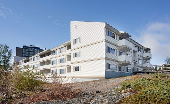 Charming apartment building with modern white facade, featuring multiple balconies and surrounded by natural landscaping under a clear blue sky.