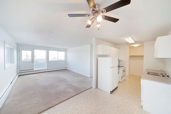 Bright open-plan living space featuring a cozy living area with large windows, modern kitchen with sleek appliances, and a stylish ceiling fan for comfort.