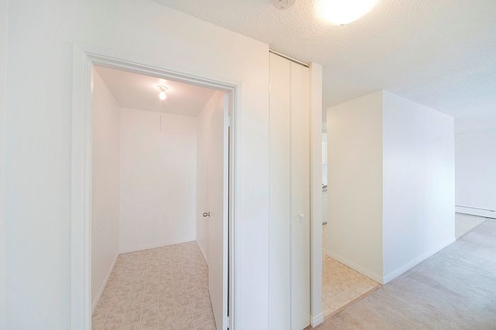 Bright and spacious apartment hallway with modern white interiors, showcasing elegant transitions from carpet to tiled flooring.