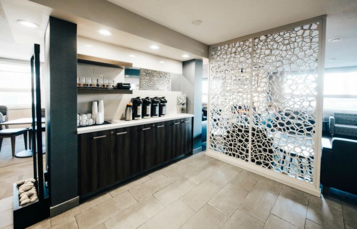Modern coffee station with stylish cabinetry and decorative partition in a bright, welcoming lounge area.