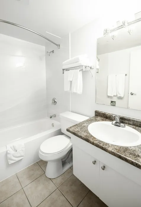 Bright, modern bathroom featuring a sleek granite countertop, elegant mirror, and pristine white bathtub.