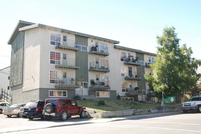 Modern three-story apartment building with charming balconies and ample parking, nestled in a vibrant, green neighborhood.