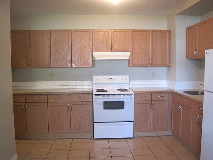 Inviting kitchen with ample wooden cabinetry, modern appliances, and sleek tile flooring.