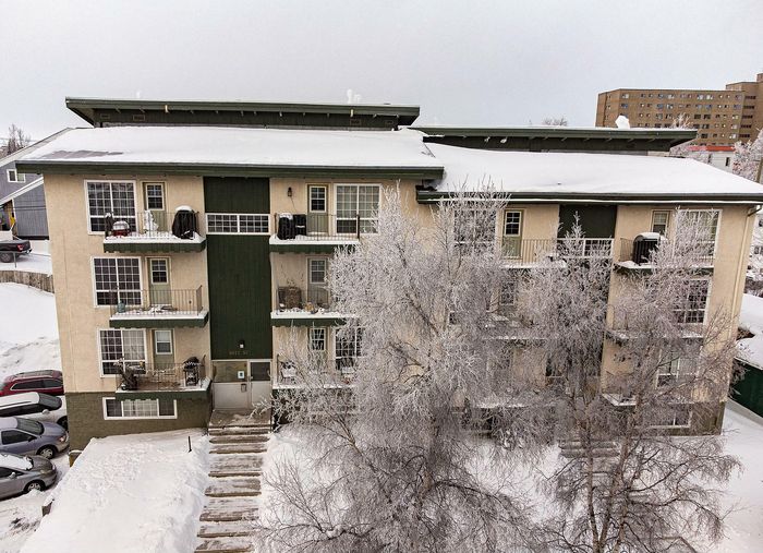 Charming apartment building with snow-covered balconies and picturesque winter setting, featuring frosted trees and a spacious entrance.