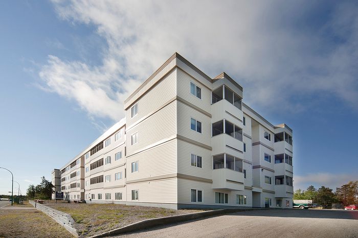 Elegant, modern apartment building with clean lines and expansive windows, set against a clear blue sky.