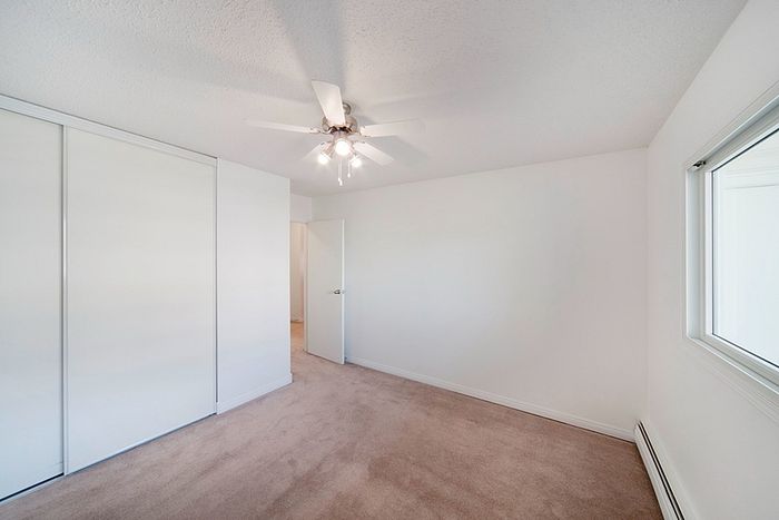 Bright bedroom featuring cozy carpet flooring, a sleek ceiling fan, and ample closet space with sliding doors.