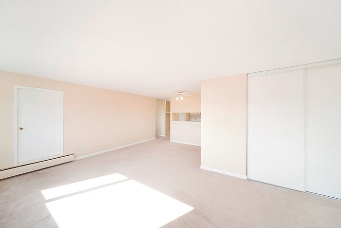 Bright and airy living space with neutral tones, expansive windows, and convenient access to kitchen area.