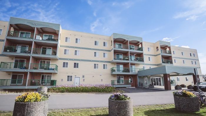 Inviting four-story apartment building with charming balconies and beautiful flower arrangements, set against a vibrant blue sky.