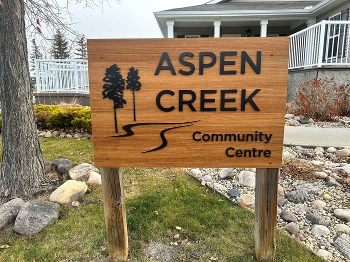 Inviting wooden sign for Aspen Creek Community Centre, surrounded by lush greenery and a charming pathway.