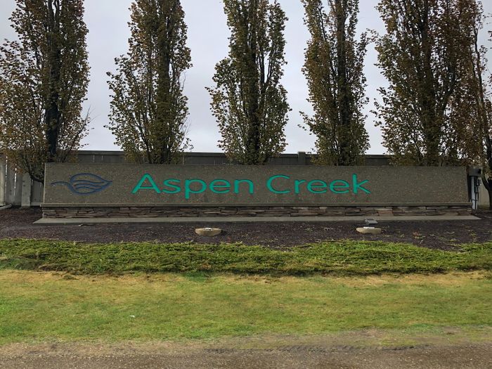 Elegant entrance sign of Aspen Creek surrounded by tall, lush trees and neatly trimmed greenery.