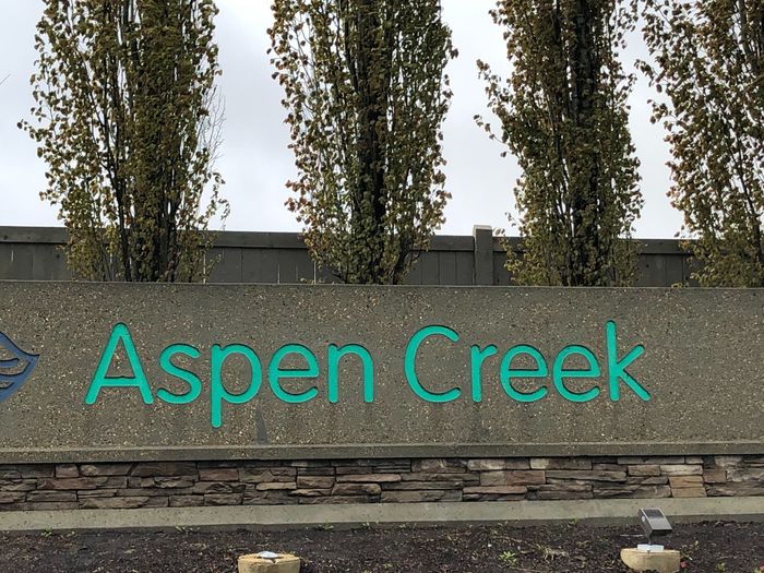 Aspen Creek entrance sign with lush trees and natural stone accents, conveying a welcoming community atmosphere.