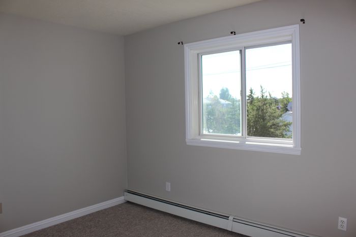 Bright and inviting room with neutral walls, large window and picturesque outdoor view, perfect for customization.