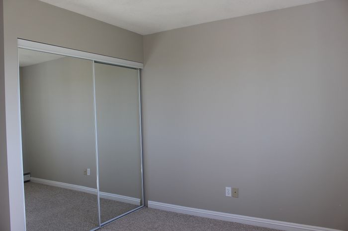 Bright, spacious bedroom with sleek mirrored closet doors and neutral walls, perfect for personalization.