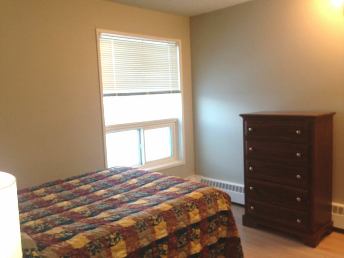Cozy bedroom with natural light, featuring a colorful quilt, elegant wooden dresser, and modern decor.