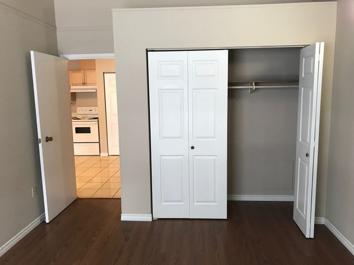 Inviting room with hardwood flooring, featuring a spacious closet and a glimpse into a modern kitchen.