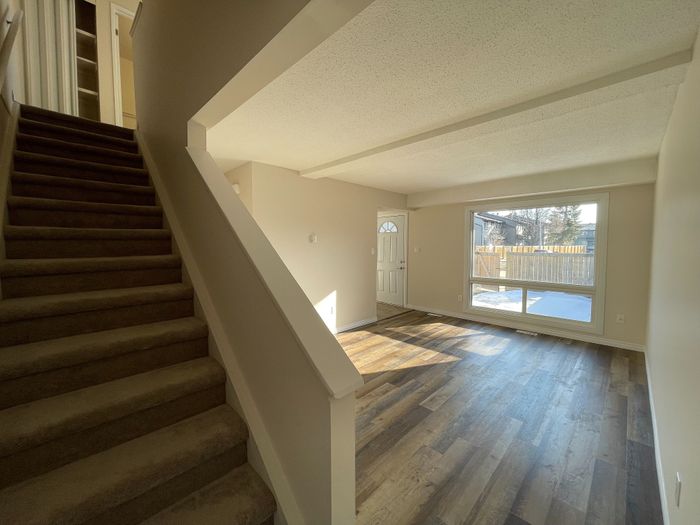 Inviting living space with elegant wooden flooring, large window allowing natural light, and carpeted stairs leading to the upper level.