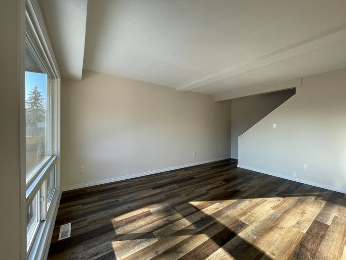 Bright living area with large windows and elegant hardwood flooring, leading to an inviting staircase.