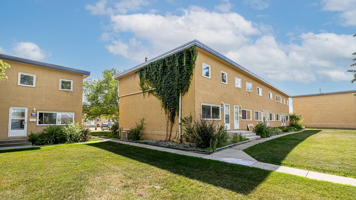 Sunlit apartment complex with charming ivy accents and spacious green lawn, perfect for comfortable living.